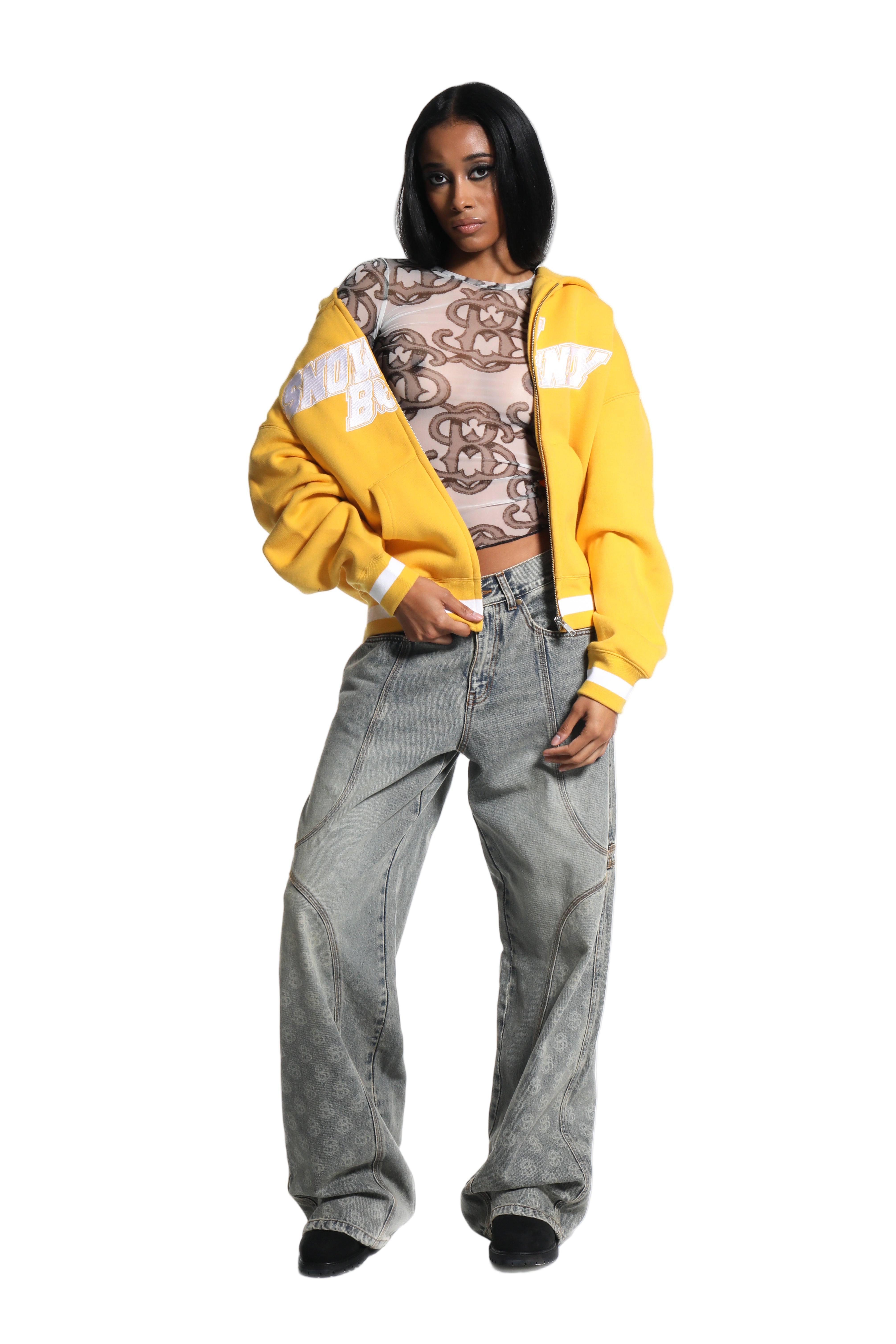 Person wearing a yellow cardigan, patterned top, and gray jeans on a white background